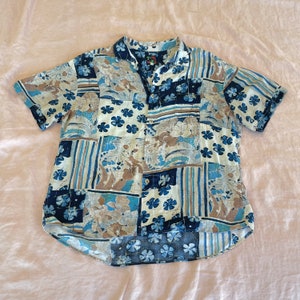 May include: A blue and white patterned short-sleeved button-up shirt with a collar. The shirt has a patchwork design with various floral and geometric patterns.