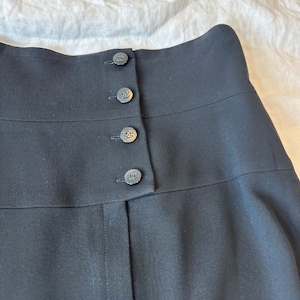 May include: Black high-waisted skirt with a row of five buttons featuring the Chanel logo.