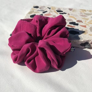 May include: A deep pink scrunchie made of soft fabric. The scrunchie is gathered into a flower shape.