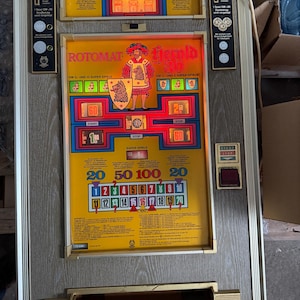 Könnte beinhalten: Vintage Rotomat Jemld 30 Spielautomat mit gelb-oranger Front, Rittergrafik und Zahlenanzeigen. Die Maschine hat einen Holzrahmen und verschiedene Knöpfe und Münzschlitze.
