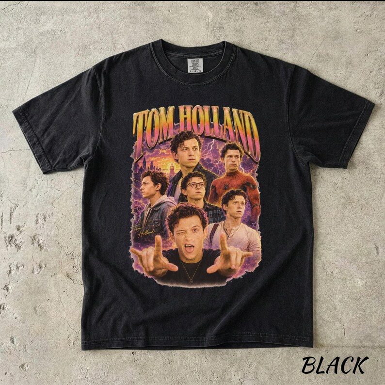 May include: Black t-shirt featuring a graphic of Tom Holland in various poses, with the name "TOM HOLLAND" in a retro font. The design includes images of the actor against a purple and orange background. The word "BLACK" is at the bottom.