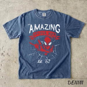 Puede incluir: Camiseta azul denim con un dise&ntilde;o desgastado de Spider-Man. El texto dice "THE AMAZING SPIDER-MAN" y "Est. '62". El dise&ntilde;o incluye una imagen roja de Spider-Man y una telara&ntilde;a.