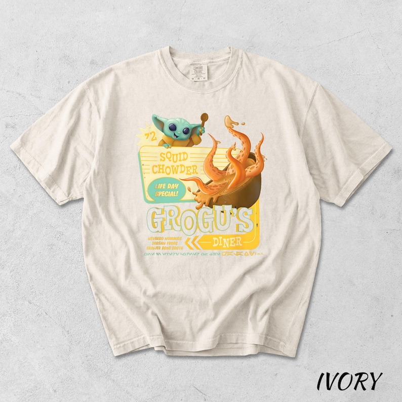 Puede incluir: Camiseta de color marfil con un dise&ntilde;o de dibujos animados. El gr&aacute;fico incluye un personaje alien&iacute;gena verde, un cuenco de tent&aacute;culos naranjas y el texto "Squid Chowder" y "Grogus Diner". La camiseta tiene cuello redondo y mangas cortas.