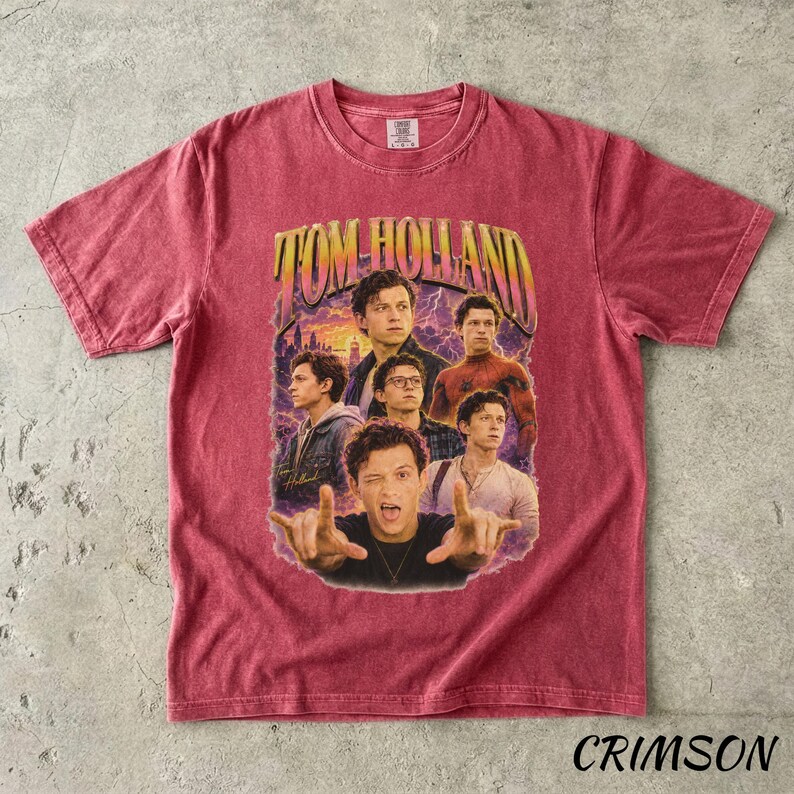 May include: Crimson-colored t-shirt featuring a vintage-style graphic of Tom Holland. The graphic includes multiple images of the actor with the text "TOM HOLLAND" in a retro font. The shirt is a crew neck.