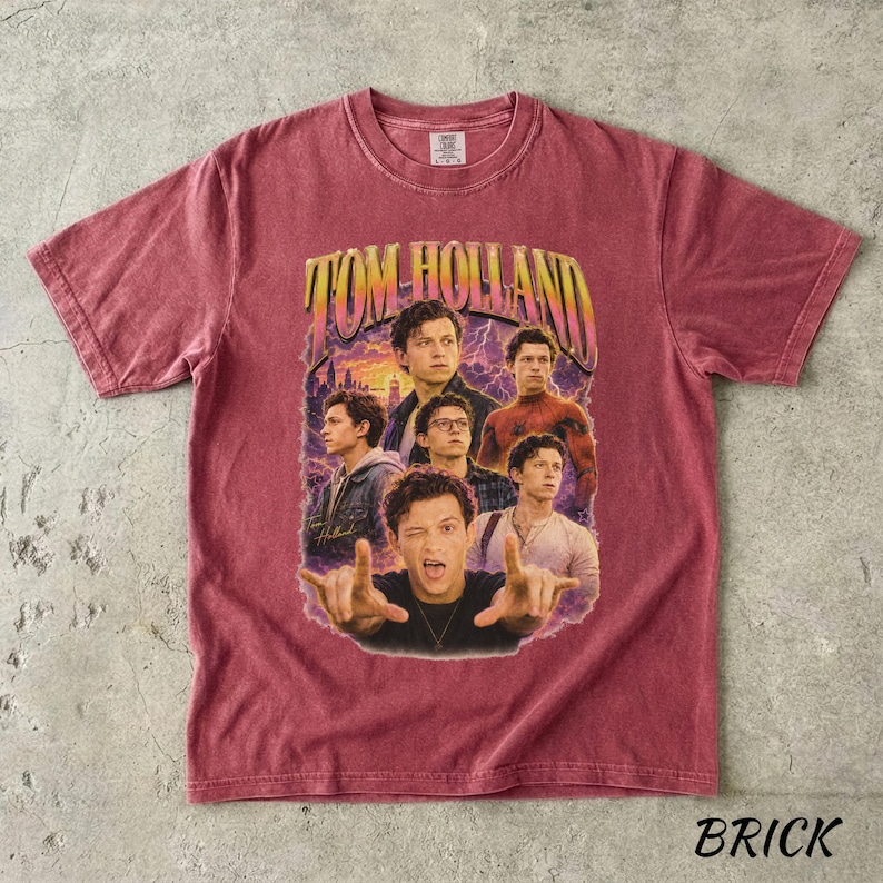 May include: Brick-colored t-shirt featuring a vintage-style graphic of Tom Holland. The graphic includes multiple images of the actor with the text "TOM HOLLAND" in a retro font. The shirt has a crew neck and short sleeves.