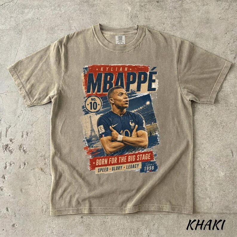 Puede incluir: Camiseta color caqui con un gr&aacute;fico de Kylian Mbapp&eacute;, futbolista, con el texto "MBAPPE" en rojo y azul. La camiseta incluye el n&uacute;mero 10 y las frases "BORN FOR THE BIG STAGE", "SPEED GLORY LEGACY" y el a&ntilde;o 1998.