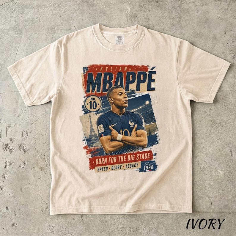 Puede incluir: Camiseta color marfil con un gr&aacute;fico de Kylian Mbapp&eacute;, futbolista. El dise&ntilde;o incluye el nombre del jugador, el n&uacute;mero 10 y el texto "BORN FOR THE BIG STAGE". La camiseta tambi&eacute;n tiene las palabras "SPEED GLORY LEGACY" y el a&ntilde;o 1998.