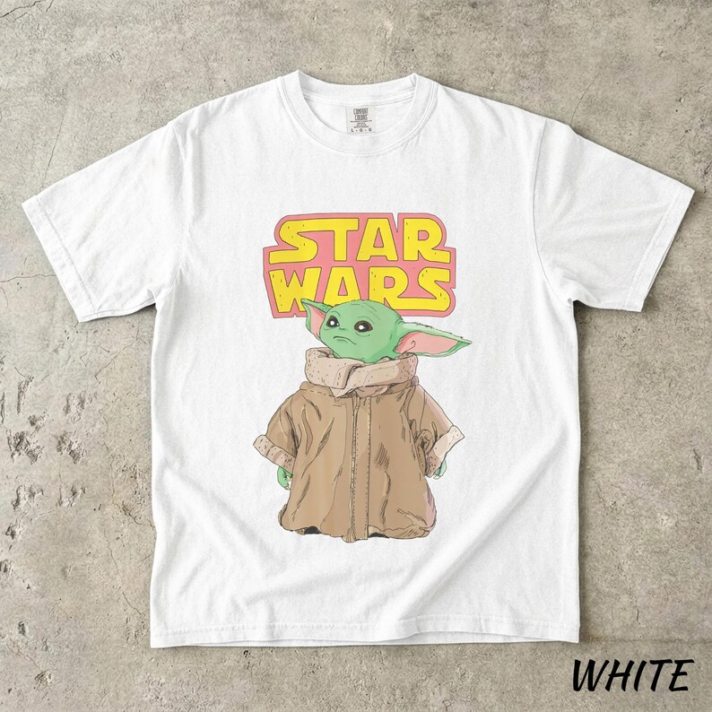 May include: White t-shirt featuring a graphic of a green alien character from Star Wars, with the text "STAR WARS" in yellow and pink. The alien is wearing a brown coat. The word "WHITE" is printed at the bottom.