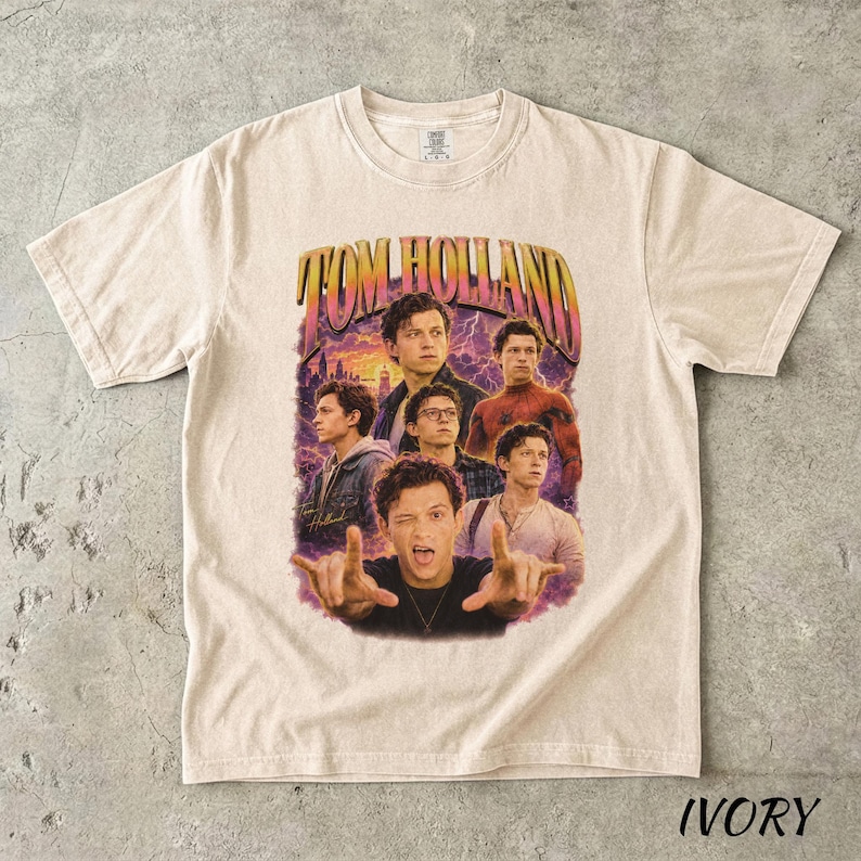 May include: Ivory-colored t-shirt featuring a graphic of Tom Holland in various poses, with the text "TOM HOLLAND" in a retro font. The design includes images of the actor against a purple and orange background.