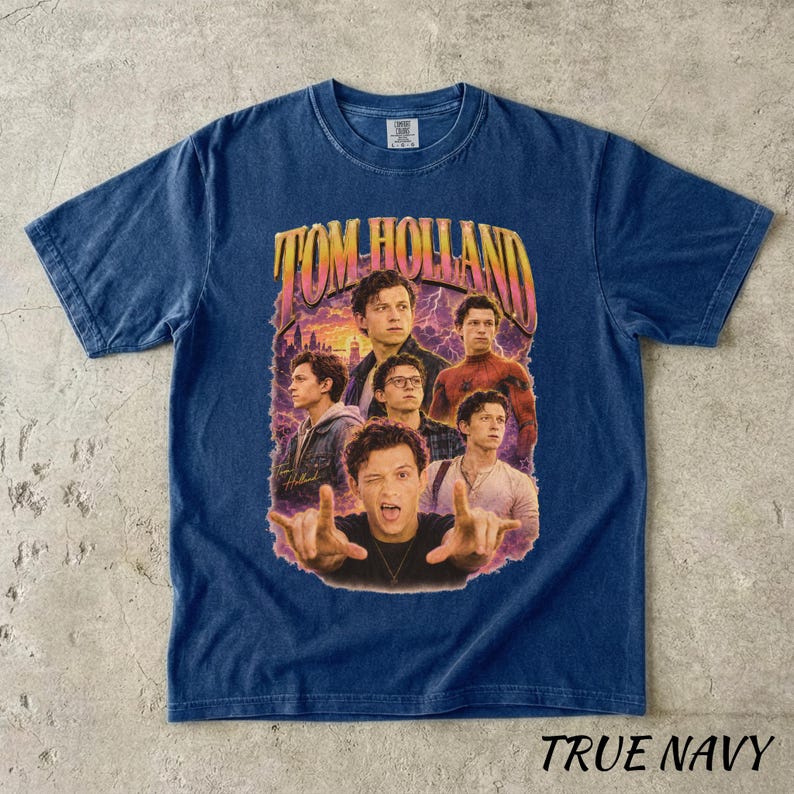 May include: A navy blue t-shirt featuring a graphic of Tom Holland with the text "TOM HOLLAND" in a retro style. The shirt has a crew neck and short sleeves. The words "TRUE NAVY" are printed at the bottom.