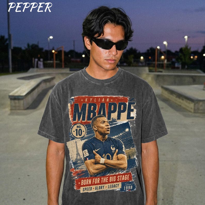 Puede incluir: Camiseta gris oscuro con un gr&aacute;fico de Kylian Mbapp&eacute;, futbolista, con el texto "KYLIAN MBAPPE" y "NO. 10". El dise&ntilde;o incluye las frases "BORN FOR THE BIG STAGE", "SPEED GLORY LEGACY" y el a&ntilde;o "1998". La marca "PEPPER" est&aacute; en la parte superior.