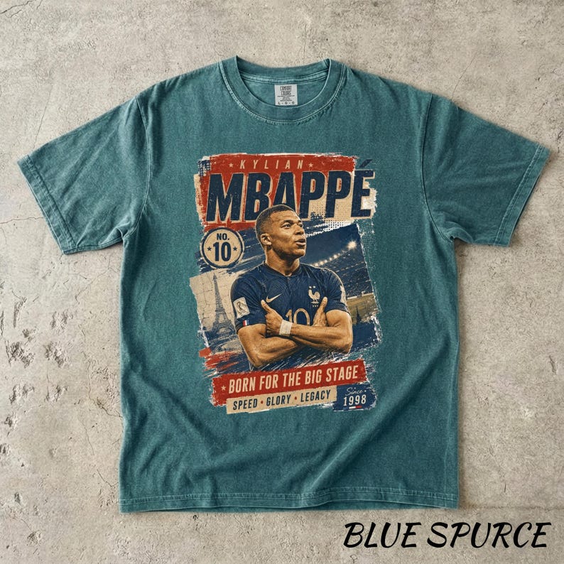 Puede incluir: Camiseta azul verdoso con un gr&aacute;fico de Kylian Mbapp&eacute;. El dise&ntilde;o incluye el texto "MBAPPE", "NO. 10" y "BORN FOR THE BIG STAGE". La camiseta tambi&eacute;n tiene el texto "SPEED GLORY LEGACY" y el a&ntilde;o "1998".