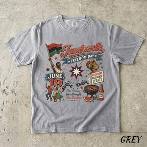 K&ouml;nnte beinhalten: Graues T-Shirt mit einem Juneteenth-Motiv. Das Design enth&auml;lt den Text "Juneteenth Freedom Day", eine Flagge und Illustrationen von Menschen, einem Grill und Wassermelone. Das Shirt hat auch den Text "Our History Our Strength Our Freedom".