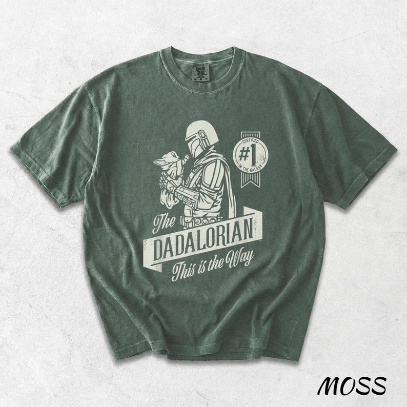 Pu&ograve; includere: T-shirt verde muschio con una grafica di The Mandalorian che tiene Grogu, con la scritta "The DADALORIAN This is the Way". La maglietta ha anche un distintivo "#1 in the Galaxy".