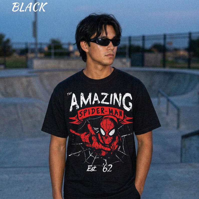 Puede incluir: Camiseta negra con un gr&aacute;fico de Spider-Man y el texto "THE AMAZING SPIDER-MAN" en blanco y rojo. El dise&ntilde;o incluye una telara&ntilde;a y el texto "Est. '62".