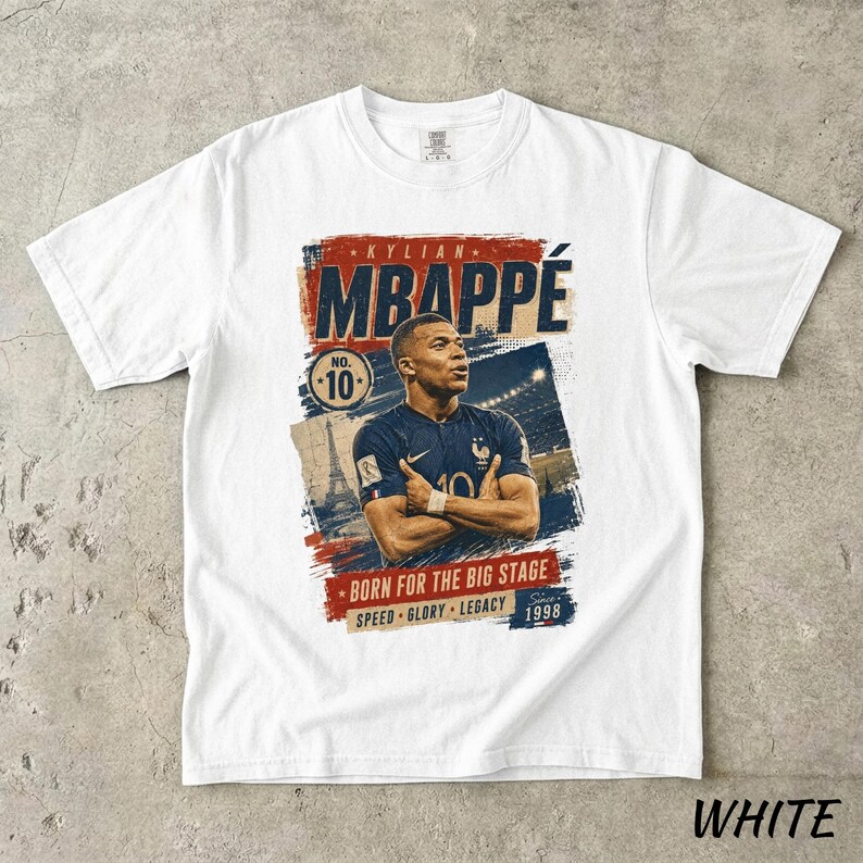 Puede incluir: Camiseta blanca con un dise&ntilde;o gr&aacute;fico de Kylian Mbapp&eacute;, futbolista, con el nombre "MBAPPE" en un lugar destacado. El dise&ntilde;o incluye el n&uacute;mero 10, la Torre Eiffel y la frase "BORN FOR THE BIG STAGE".