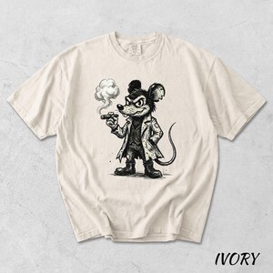 May include: Ivory-colored t-shirt featuring a black and white illustration of a mouse smoking a cigar. The mouse is dressed in a coat and hat, with a stern expression. The word "IVORY" is printed at the bottom of the shirt.