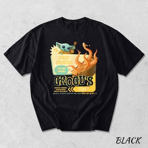 Puede incluir: Camiseta negra con un dise&ntilde;o de dibujos animados de Grogu's Diner. El gr&aacute;fico incluye a Grogu, un cuenco de sopa de calamares y el texto "Squid Chowder, Life Day Special!". La camiseta tambi&eacute;n presenta el texto "Grogu's Diner" en un estilo retro.