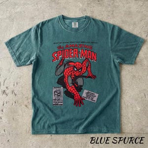 May include: Blue Spruced t-shirt featuring a comic book style graphic of Spider-Man. The design includes the text "The Amazing Spider-Man" in red and white, along with comic book panels. The shirt is a short-sleeved crew neck.