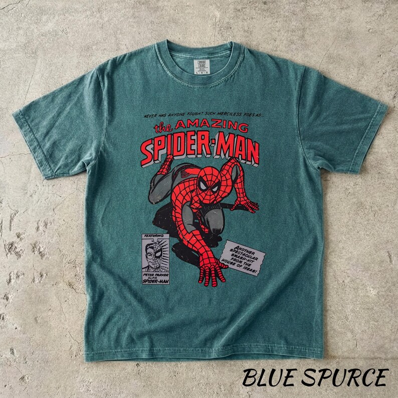 May include: Blue Spruced t-shirt featuring a comic book style graphic of Spider-Man. The design includes the text "The Amazing Spider-Man" in red and white, along with comic book panels. The shirt is a short-sleeved crew neck.