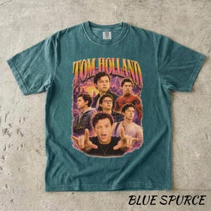 May include: Teal-colored t-shirt featuring a graphic of Tom Holland with the text "TOM HOLLAND" in a retro style. The shirt has a vintage wash and the words "BLUE SPURCE" are printed at the bottom.
