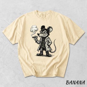 May include: Banana-colored t-shirt featuring a black and white cartoon illustration of a mouse smoking a cigar. The mouse is dressed in a coat and boots. The word "BANANA" is printed in black at the bottom of the shirt.