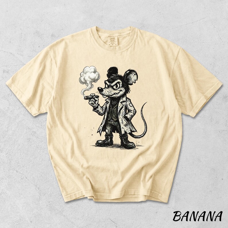 May include: Banana-colored t-shirt featuring a black and white cartoon illustration of a mouse smoking a cigar. The mouse is dressed in a coat and boots. The word "BANANA" is printed in black at the bottom of the shirt.