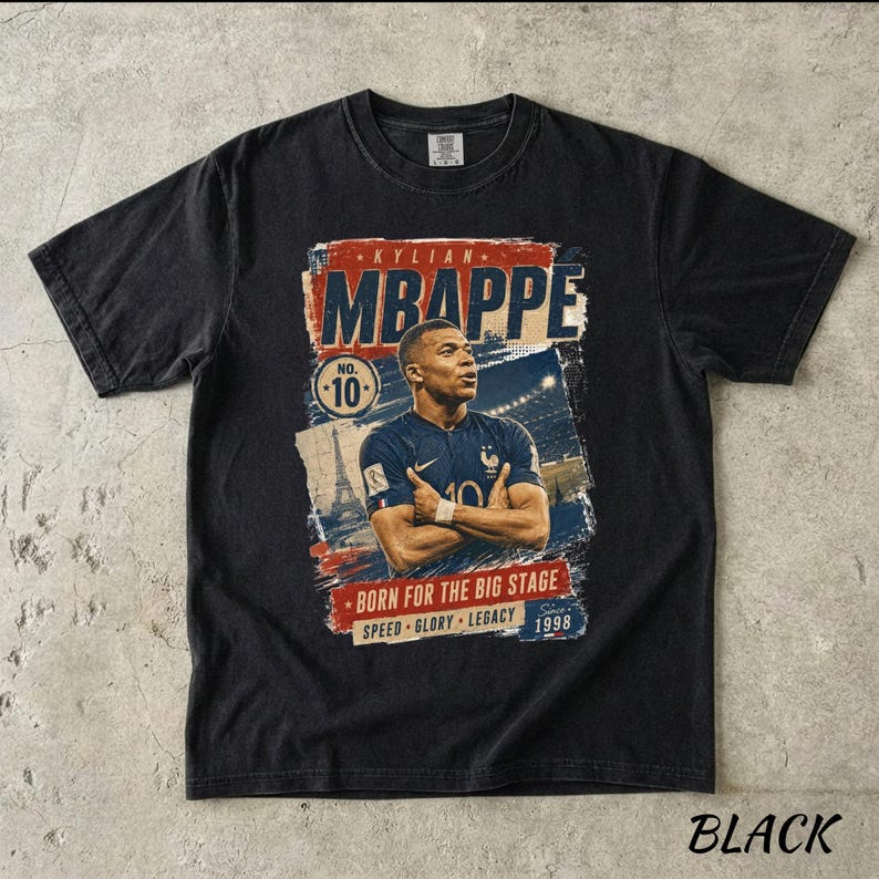 Puede incluir: Camiseta negra con un gr&aacute;fico de Kylian Mbapp&eacute;, con el texto "MBAPPE" en rojo y azul. El dise&ntilde;o incluye el n&uacute;mero 10, la Torre Eiffel y las palabras "BORN FOR THE BIG STAGE". La camiseta tambi&eacute;n tiene el texto "SPEED GLORY LEGACY 1998".