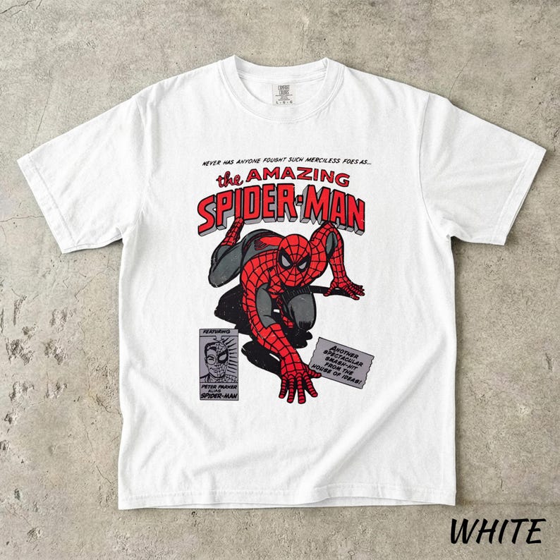 May include: White t-shirt featuring a comic book illustration of Spider-Man. The design includes the text "the AMAZING SPIDER-MAN" in red and black, with additional comic book panels and text. The shirt is a classic crew neck.