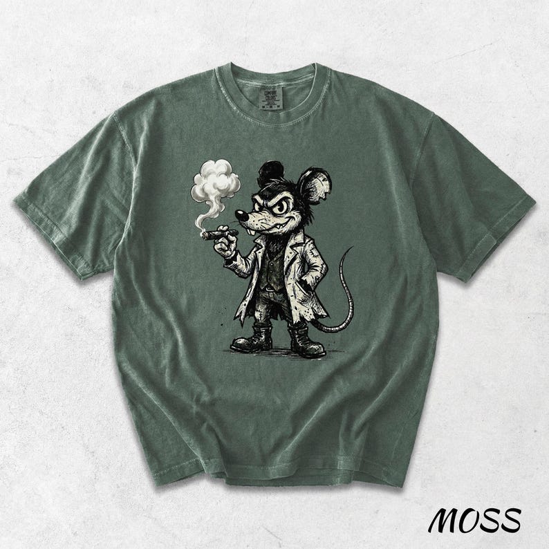 May include: Moss green t-shirt featuring a cartoon mouse smoking a cigar. The mouse is dressed in a coat and boots, with a stern expression. The shirt has a crew neck and short sleeves. The word "MOSS" is printed at the bottom right.