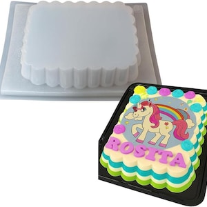 Puede incluir: Un molde de gelatina cuadrado y transparente con borde festoneado se encuentra sobre un pastel decorado. El pastel presenta un dise&ntilde;o de unicornio con un arco&iacute;ris y el nombre "Rosita" en letras rosas.
