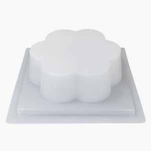 May include: A white, flower-shaped mould for baking or crafting. The mould is made of a smooth, glossy material and sits on a square base. The flower shape has rounded petals and is elevated above the base.