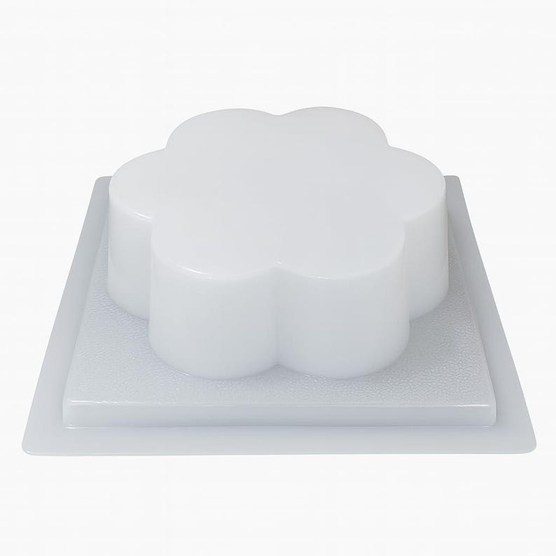 May include: A white, flower-shaped mould for baking or crafting. The mould is made of a smooth, glossy material and sits on a square base. The flower shape has rounded petals and is elevated above the base.