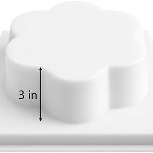 May include: A white, flower-shaped object, 7.6 cm tall, sits on a square base. The object has rounded edges and a smooth surface. The base is also white and square. The image is a product shot, likely for a mold or similar item.