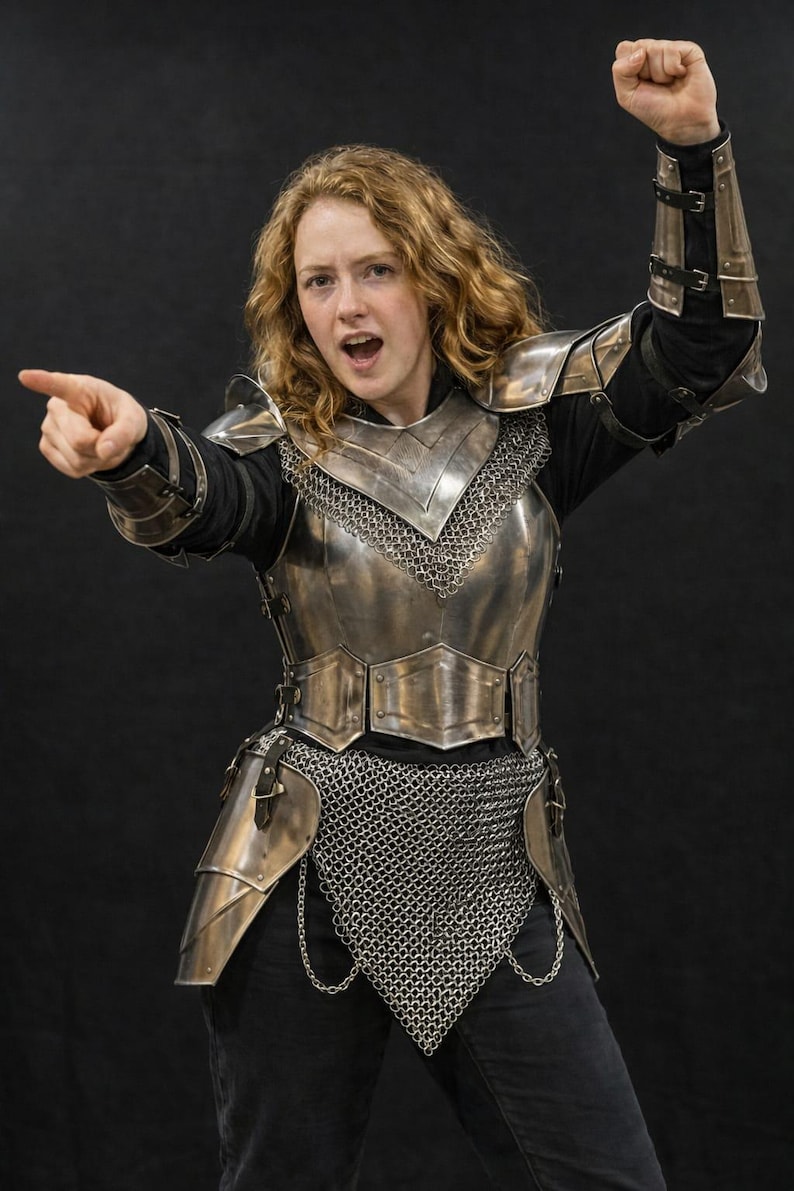 May include: A suit of polished steel plate armor featuring a breastplate, pauldrons, and vambraces worn over a black long-sleeve shirt. The armor includes a chainmail hauberk, tassets, and leather straps with metal buckles, providing full torso coverage.