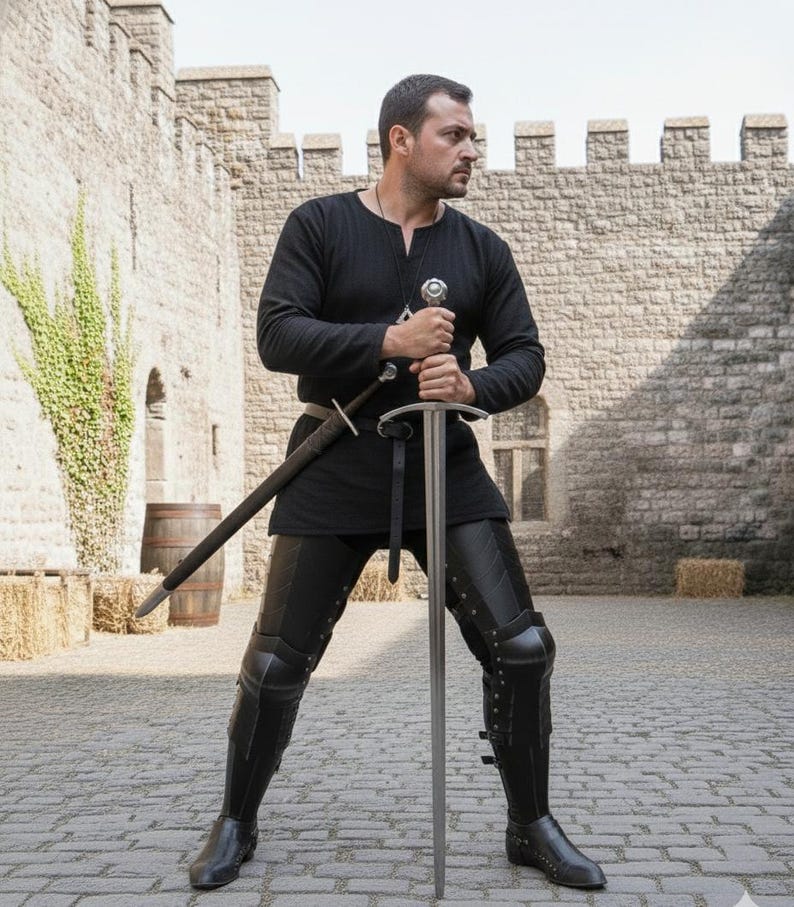 Puede incluir: Una persona con atuendo medieval negro, sosteniendo una espada larga. El atuendo incluye una t&uacute;nica de manga larga, pantalones de cuero y armadura para las piernas. Una segunda espada est&aacute; enfundada en la cintura. El fondo presenta un castillo de piedra.