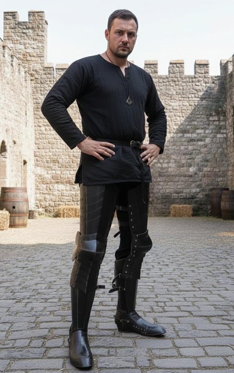 Puede incluir: Una persona con armadura medieval negra, que incluye protecci&oacute;n para piernas y rodillas, y una t&uacute;nica negra. La armadura parece ser de cuero y metal. La persona est&aacute; de pie sobre una superficie adoquinada.