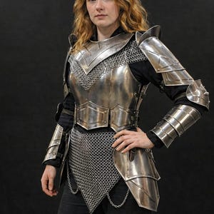 May include: A polished steel plate armor set featuring a breastplate, pauldrons, and articulated arm guards. The armor includes integrated chainmail sections at the neck and waist, with leather straps and buckles securing the metal components.