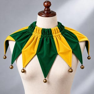 May include: A collar featuring alternating yellow and green fabric panels in a pointed, star-like design. The neckline is gathered with elastic, and each of the six points is finished with a small, round, metallic bronze-coloured bell.