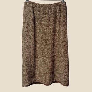 May include: A brown midi-length skirt featuring a dense, all-over pattern of tiny white dots. The skirt has a straight, simple silhouette with a clean hemline and a waistband, presented hanging from a black hanger against a plain background.