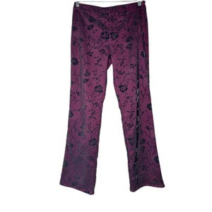 May include: Plum-colored pants with a floral pattern in black. The pants have a straight leg cut and are hanging on a metal hanger. The floral design covers the entire surface of the pants.