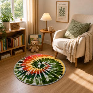 K&ouml;nnte beinhalten: Ein runder Tie-Dye-Teppich mit einem Spiralmuster in Rot, Orange, Gelb, Gr&uuml;n und Wei&szlig;. Der Teppich liegt auf einem Holzboden in einem Wohnzimmer, zusammen mit einem cremefarbenen Sessel und einem kleinen Beistelltisch.
