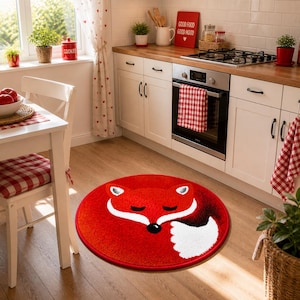 K&ouml;nnte beinhalten: Ein runder, roter Teppich mit einem wei&szlig;en und schwarzen Fuchsmotiv. Er liegt auf einem Holzboden in einer K&uuml;che. Die K&uuml;che hat wei&szlig;e Schr&auml;nke, einen Herd und ein Fenster.