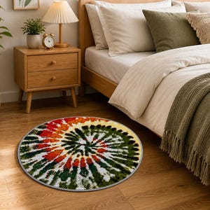K&ouml;nnte beinhalten: Ein runder Tie-Dye-Teppich mit einem Spiralmuster in Rot-, Gr&uuml;n-, Gelb- und Wei&szlig;t&ouml;nen. Der Teppich liegt auf einem Holzboden in der N&auml;he eines Bettes mit wei&szlig;er Bettw&auml;sche und einem Nachttisch aus Holz.