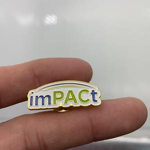 May include: A gold-toned metal lapel pin featuring the word imPACT in a mix of blue and green enamel lettering. The design includes a white background with a thin curved line above the text and a small arrow pointing upward from the letter i.