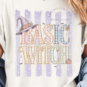 Può includere: Una t-shirt a maniche corte color crema con una stampa grafica che riporta il testo BASIC WITCH. Il design include un cappello da strega viola, una piccola zucca e pipistrelli su uno sfondo a strisce verticali viola con pois bianchi.