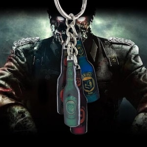 May include: A keychain featuring four bottle-shaped charms with various labels and colors, including green, blue, and red. The charms are attached to a silver keyring. The background shows a blurred image of a zombie.