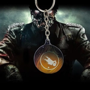 May include: A round keychain with a silver chain and ring. The keychain has a circular, transparent pendant with a graphic of a person falling, set against a yellow and orange background. The background features a zombie in a military uniform.