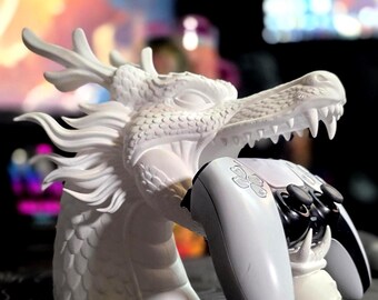 Può includere: Una scultura a testa di drago bianca con squame dettagliate e criniera fluente, progettata come supporto per un controller per videogiochi bianco e nero. La bocca aperta e l'artiglio del drago tengono il controller in posizione orizzontale.