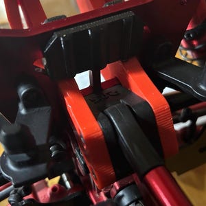 Pode incluir: Close-up de um componente mecânico vermelho e preto, possivelmente para um veículo ou modelo. O design apresenta uma combinação de peças vermelhas e pretas, com parafusos e juntas visíveis. A estrutura geral parece robusta e intrincada.